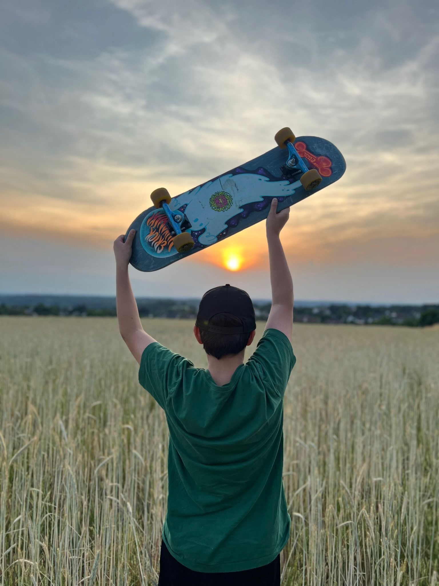 Jugendlicher mit Skateboard im Feld bei Sonnenuntergang